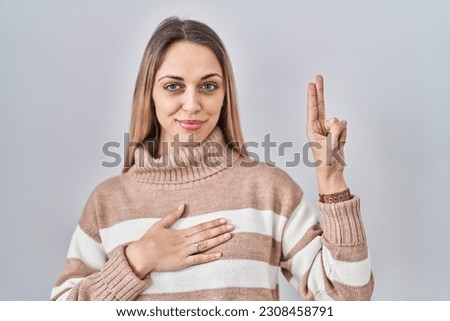 Young blonde woman wearing turtleneck sweater over isolated background smiling swearing with hand on chest and fingers up, making a loyalty promise oath 