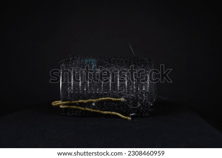 black hair roller and two gold grips isolated on a black background laying on its side