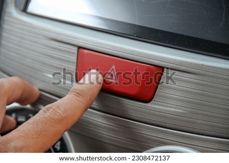 a man's index finger is pressing a red button on a car dashboard.