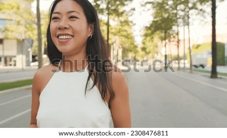 Cute happy girl dressed in white top and jeans walks along the street of modern city