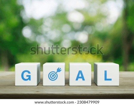 Goal icon on white block cubes on wooden table over blur green tree in park, Business success concept