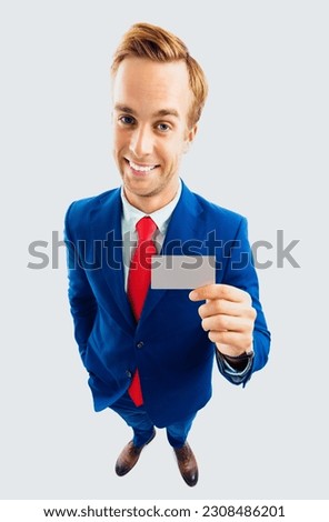 Full body portrait of funny businessman in blue confident suit and red tie, showing blank business or plastic credit card, with copyspace area for text or slogan, top angle view shot isolated on grey