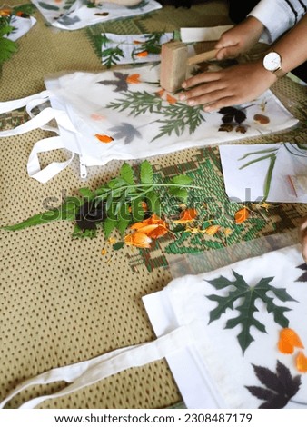 Hands in frame making botanical print or ecoprint with wooden hammer and it called pounding method on canvas totebag. Natural dyes for organic fabric.                                