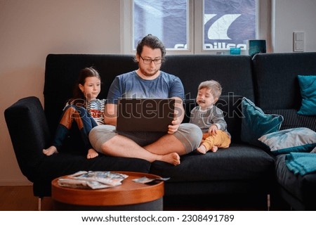 Young dad sits with his children looking in laptop while sitting on dark sofa
