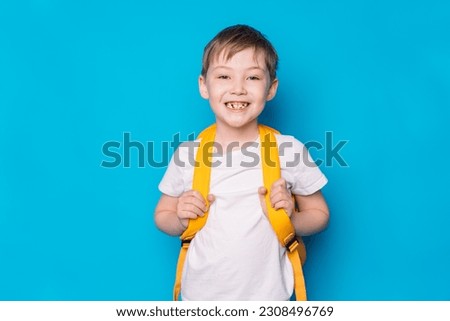 Boy with a yellow backpack against a blue background.