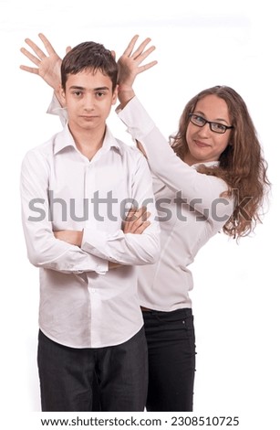 Portrait of cute schoolchildren. A girl and a guy in school clothes are having fun and joking, playing tricks on each other. The girl shows the horns.