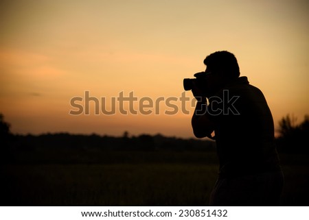 Silhouette of photographer hand holding camera with lens at sunset