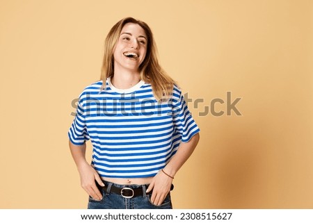 Portrait of young beautiful girl in striped shirt posing, cheerfully laughing, feeling happiness against yellow studio background. Concept of youth, human emotions, facial expression Royalty-Free Stock Photo #2308515627