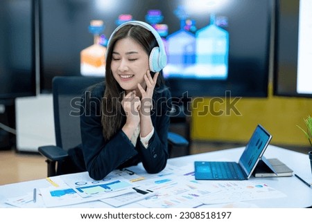 Asia business woman relaxing and listening music on the headphones while enjoying a break to stretch with hands behind her head in an office alone at work.