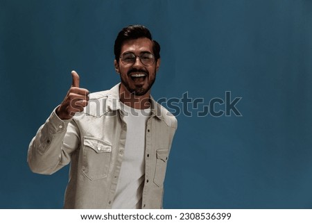 Portrait of a stylish man smile with teeth and happiness in glasses for farsightedness and myopia, on a blue background in a white T-shirt, space space Royalty-Free Stock Photo #2308536399