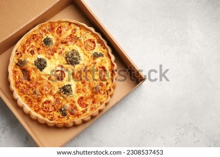 Delicious homemade vegetable quiche in carton box on light gray table, top view. Space for text