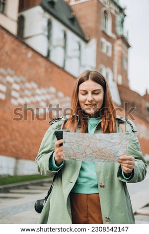 Happy optimistic woman smiling confident holding city map and smartphone at street. Attractive young female tourist is exploring new city. Traveling Europe in spring, old town. Urban lifestyle banner