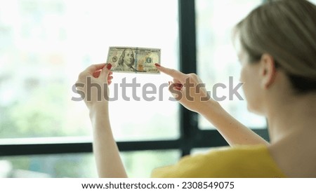 Woman studying watermarks on money dollars in front of window closeup