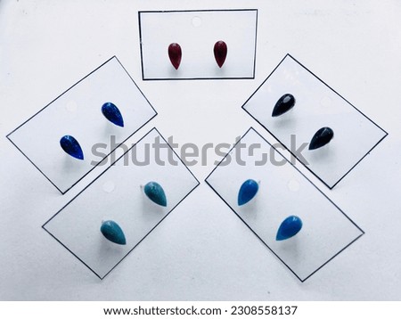 Five couple of earrings on white background. It has ten small earrings. They attached to five transparent cards. They has water drop shape and they have different colours. They made of resin material.
