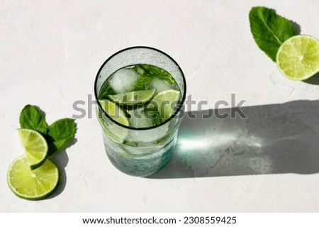Summer refreshing cocktail Mojito with rum, mint, lime and ice in glass on a white stone background and hard light with long shadows. Virgin Mojito is a summer non-alcoholic cocktail.  Royalty-Free Stock Photo #2308559425