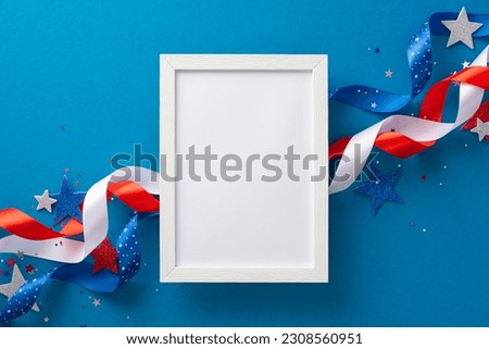 Festive arrangement depicting USA's Independence Day celebration: curly ribbons, glitter stars, confetti, and empty photo frame. Top view on a blue background with an empty frame for text or picture