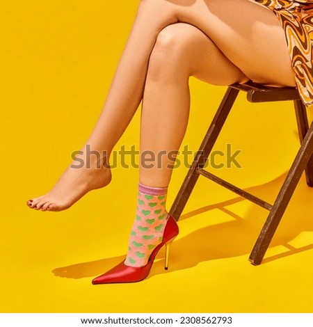 Cropped image of female slender legs on heeled shoe and funny socks against bright yellow background. Concept of pop art photography, creative vision, imagination, sales, fashion, style