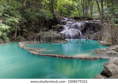 Image of the emerald, green waterfall in the forest with tall and fertile trees and shade for relax. There is water flowing down into small and large pools in layers. Make Look fresh and comfortable.