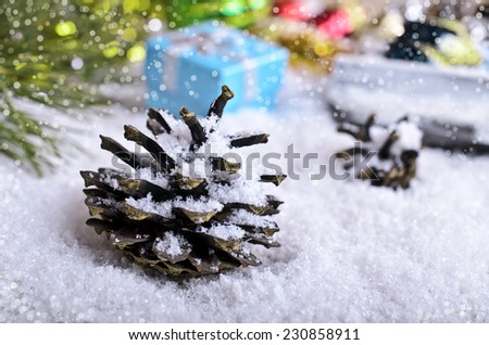 Fir cone in the snow on the background of Christmas decorations and gifts