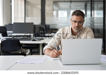 Middle-age Hispanic man using laptop computer for business studying, watch online virtual webinar training meeting, video call. Focused mature Indian or Latin businessman work in office, copy space. Royalty-Free Stock Photo #2308603395