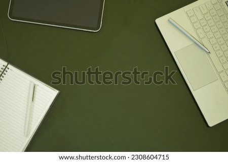 Electronics items on a table along with a notebook and pens. Picture contains a tablet, a laptop with touch pencil, writing notebook with a white pencil.