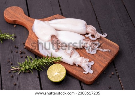 Fresh squid or raw squid on a wooden board with ingredients of Green rosemary. Lemon. Seafood menu on wooden background. Top view.