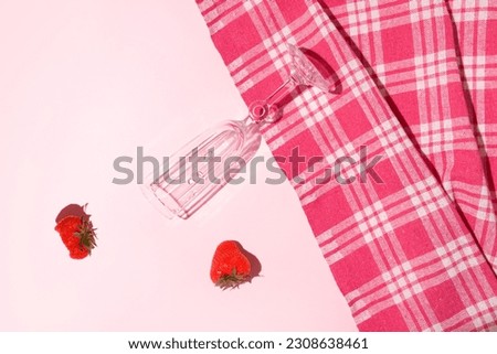 Champagne flute glass , checkered pattern table cloth and fresh strawberries, creative romantic  summer fruit layout, candy pink background. Minimal picnic idea. 