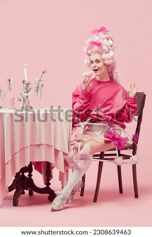 Yummy lunch. Portrait gorgeous princess, queen wearing big pink wig holding donut with exciting face on pink studio background. Comparison of eras, modernity and renaissance, beauty, food, diet, ad Royalty-Free Stock Photo #2308639463