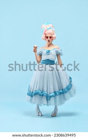 Portrait with princess, queen wearing elegant dress holding ice cream with surprised face over blue background. Concept of comparison of eras, modernity and renaissance, baroque style, beauty, fashion Royalty-Free Stock Photo #2308639495