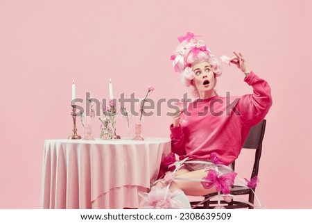 Sweet cocktails. Portrait gorgeous queen wearing big pink wig holding wine glass with exciting face over pink studio background. Comparison of eras, modernity and renaissance, beauty, history concept