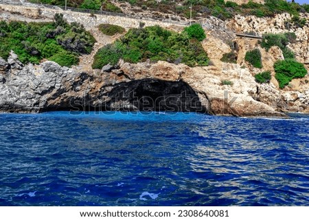 A grotto in a rock under the highway to Alanya (Turkey) - view from the sea. Large cave with concrete blocks inside against the background of mountains and blue water