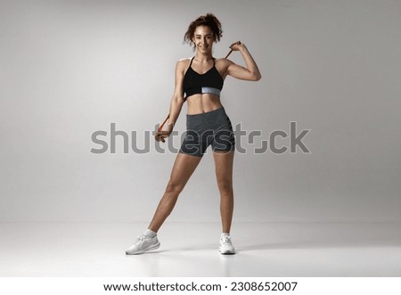 Portrait of young girl in sportswear with musuclar body posing with fitness expanders against gray studio background. Concept of sportive lifestyle, beauty, body care, fitness, health Royalty-Free Stock Photo #2308652007