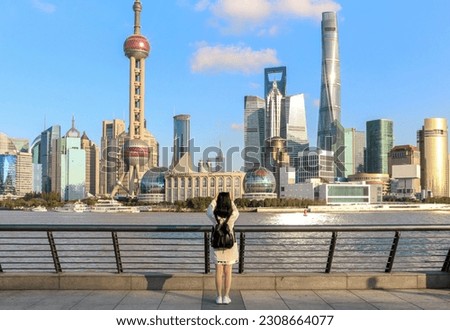 Female tourist on the Shanghai Bund taking a picture of the iconic Shanghai skyline view of Lujiazui. Shanghai a massive international city in China.