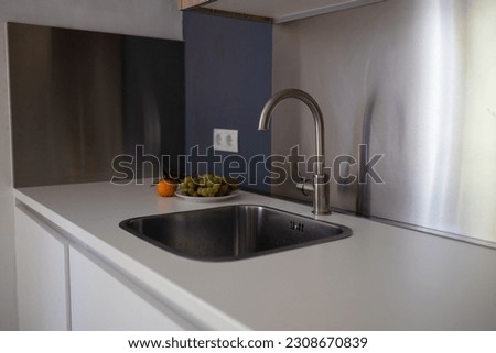 Metal kitchen sink and tap water in the kitchen. Interior of the kitchen area of the apartment. Built-in appliances. Kitchen appliances. Home Appliances. Fruit food on the table. High quality photo Royalty-Free Stock Photo #2308670839