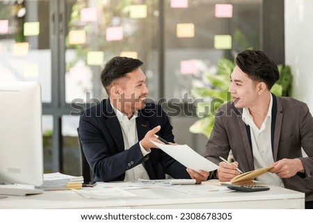 Smiling young businessman discussing something positive with his mature colleague, and using a digital tablet together