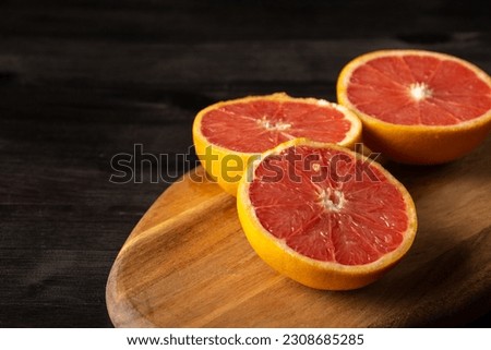 Top view of cut grapefruits on wooden board and dark table, horizontal, with copy space