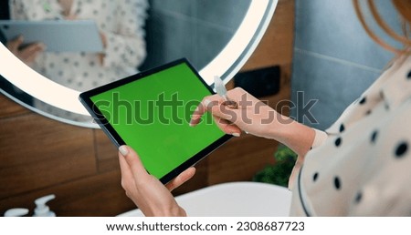 Close-up of female hands using black tablet with green screen on bathroom at home. View from the back. Chroma key