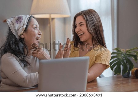 Portrait of a beautiful young Asian woman smiling and hugging her middle aged mom or grandmother, spending time at home together. Happy family bonding concept