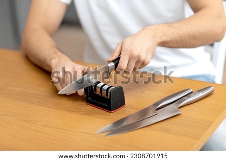 Close-up photo of man sharpening knives with special knife sharpener at home Royalty-Free Stock Photo #2308701915
