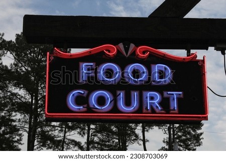 Vintage Neon Food Court Sign Outdoors With Trees in Background 
