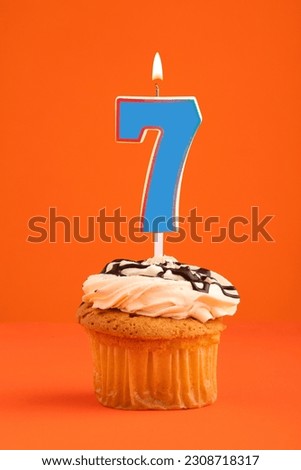 Blue number 7 candle - Birthday cake on orange background.