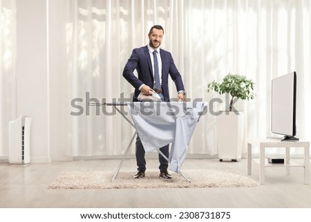 Businessman ironing a shirt at home in front of tv
