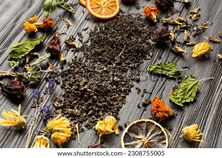 Composition of dry black and green tea, dried citrus slices, mint leaves and dry hibiscus, calendula, lavender flowers on a dark wooden background top view close-up.