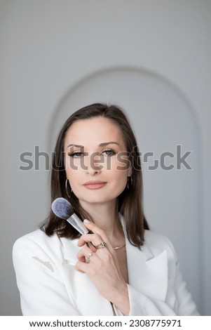 Fashion and beauty, stylish makeup artist in a white jacket with makeup brushes in her hands, business portrait of a makeup artist stylist or director of a beauty studio