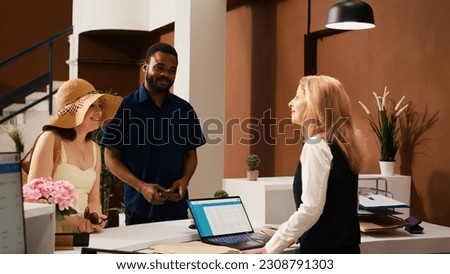 Hotel concierge greeting tourists at reception upon their arrival, welcoming guests at luxury tropical resort. Receptionist preparing to check in guests, providing excellent service. Royalty-Free Stock Photo #2308791303