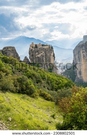 View from afar of the monastery built on the top of the vertical mountain in a blur foreground of trees and blur background of the mountain from behind