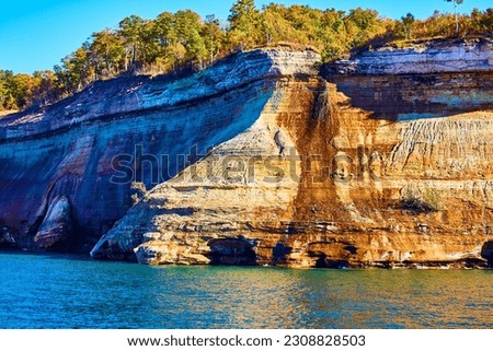 Forest above Pictured Rocks cliff with archway through stone and calm lake water