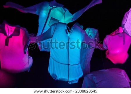 Glowing clothes of neon blue and pink hanging in the air suspended over a black background