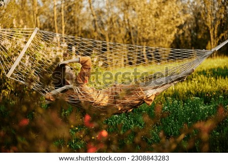a beautiful woman is resting in nature lying in a mesh hammock in a long orange dress looking to the side, propping her head with her hand. Horizontal photo on the theme of recreation