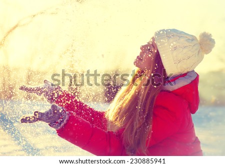 Beauty Winter Girl Blowing Snow in frosty winter Park. Outdoors. Flying Snowflakes. Sunny day. Backlit. Beauty young woman Having Fun in Winter Park. Good mood 